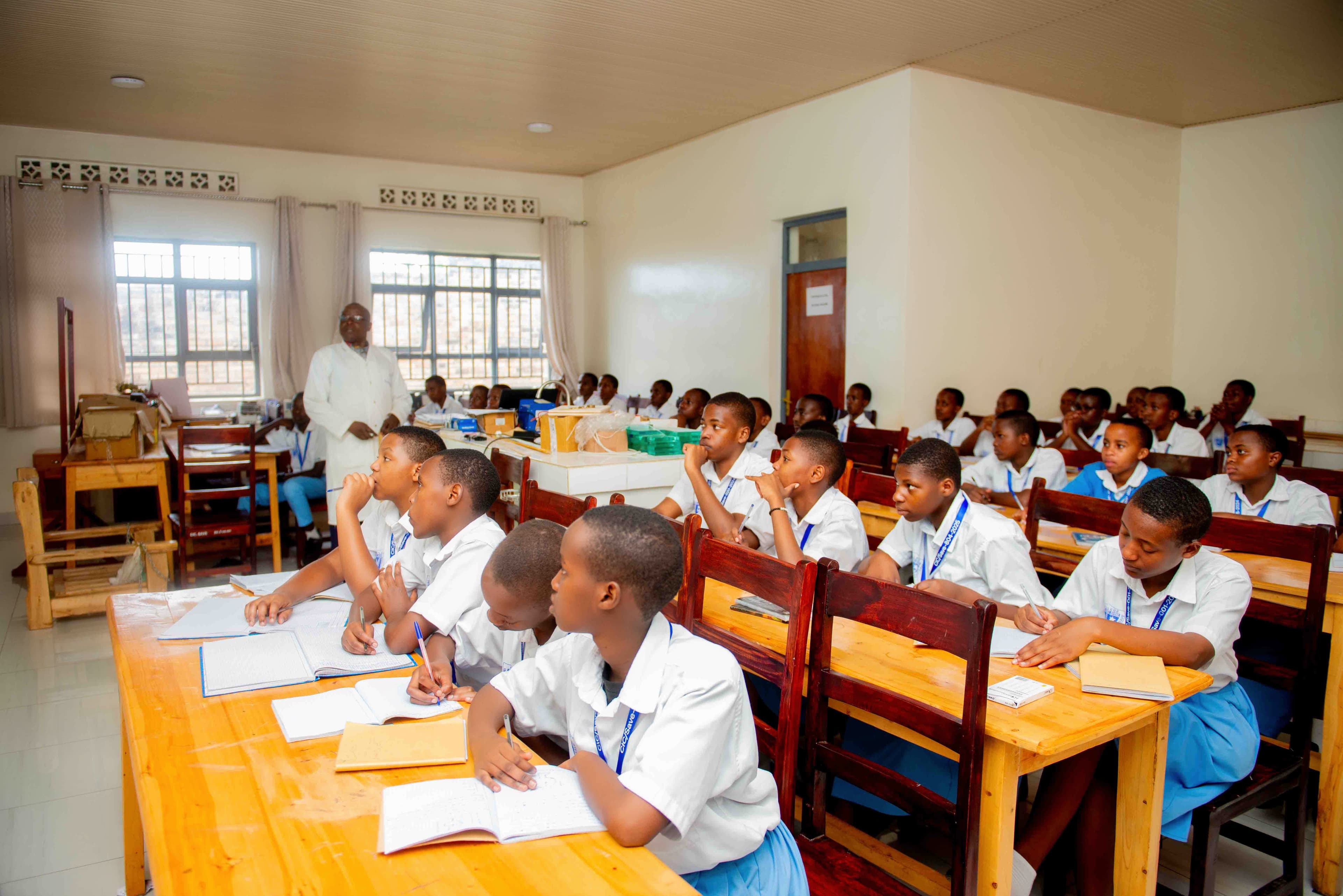 Students in a classroom, focused, with books open and a teacher guiding at the front.